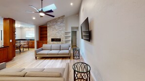 Ein modernes Wohnzimmer mit einer Couch, einem an der Wand montierten Fernseher und einem Deckenventilator.