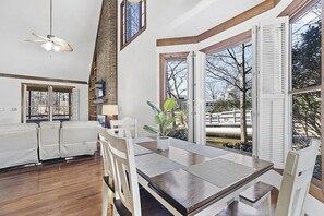 Ein Essbereich mit Holztisch und -stühlen, einem Deckenventilator und großen Fenstern mit Rollläden.