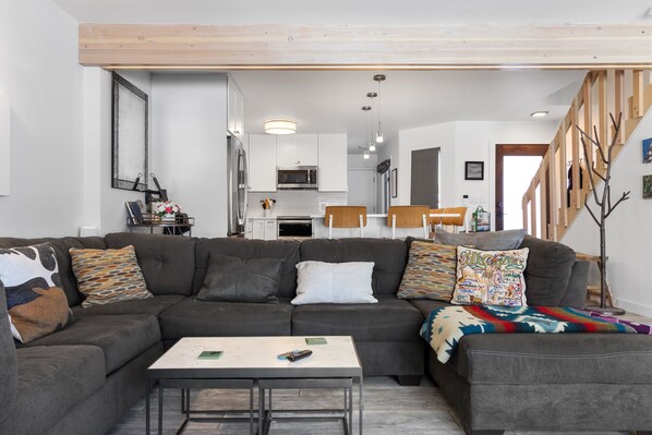 Una sala de estar moderna con un sofá seccional, una mesa de centro y una escalera que lleva a un nivel superior.
