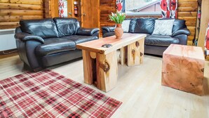 Interior d'una cabana de fusta amb dos sofàs de cuir, una taula de centre de fusta, una catifes de vellesa i una finestra amb cortines.