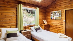 Un dormitori de cabana de fusta amb dos llits, una finestra amb cortines, una taula de nit amb una làmpada i una col·lecció de fotos penjades a la paret.