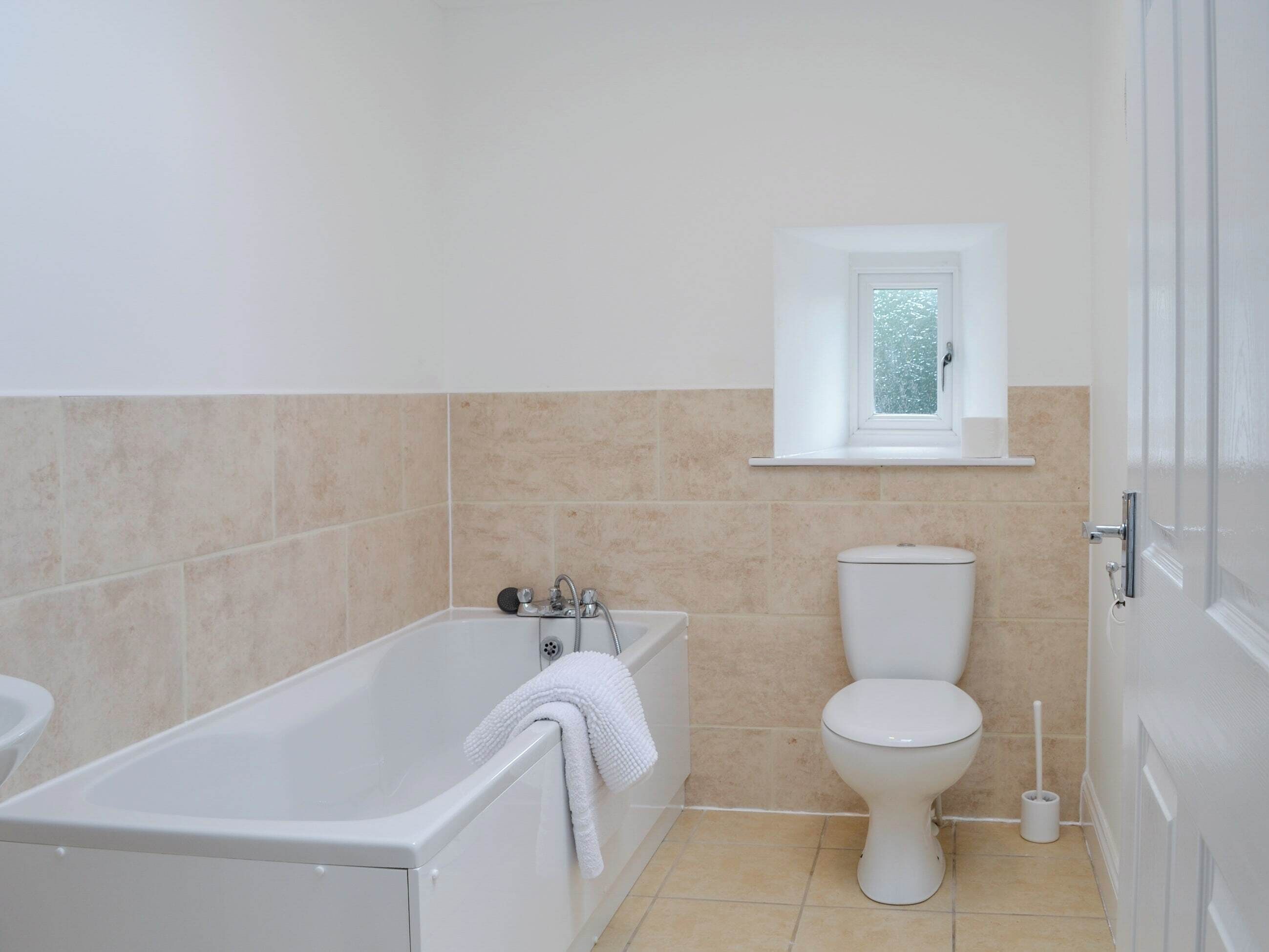 Een badkamer met een bad, toilet en een raam boven het toilet.