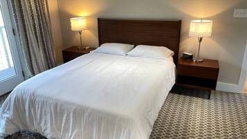 Ett hotellrum med en stor säng, två sängbord med lampor, en mönstrad matta och ett fönster med gardiner.