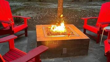 A fire pit with red chairs arranged around it on a patio.