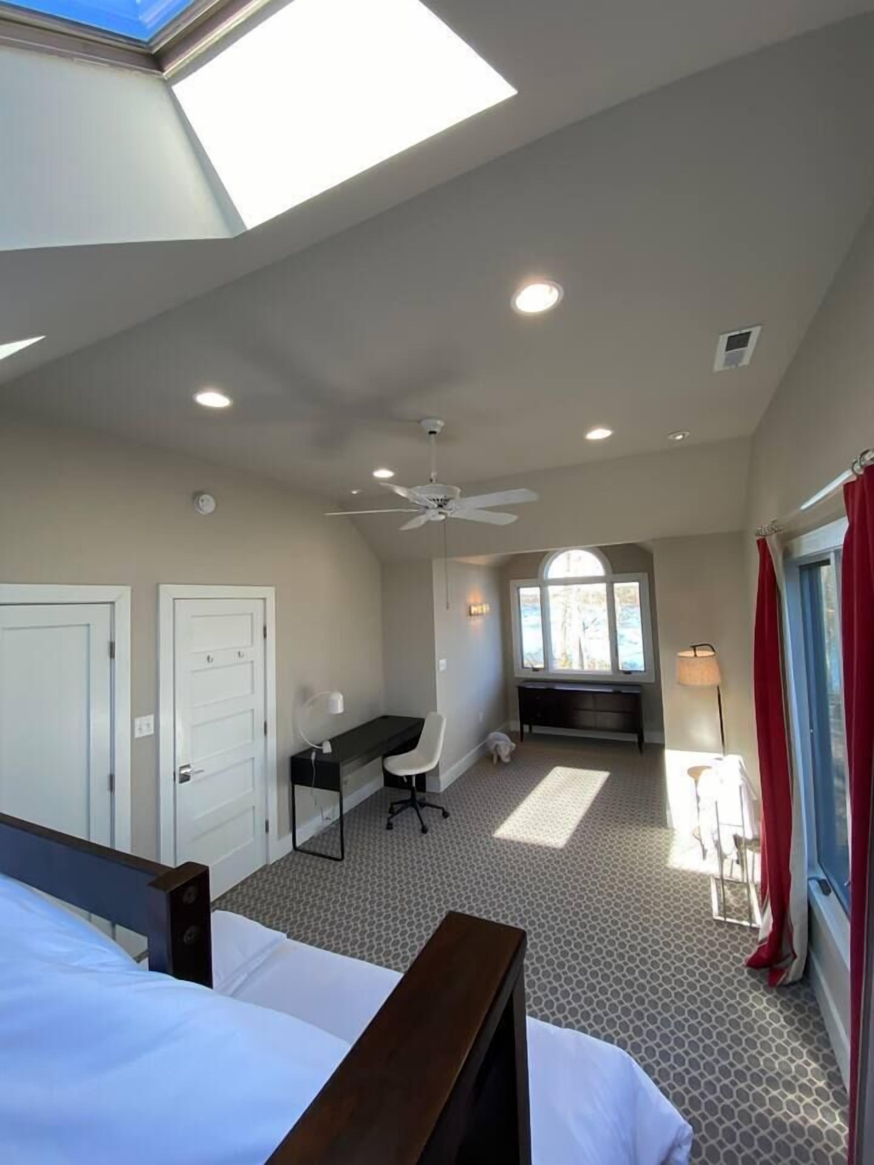 A bedroom with a skylight, a desk, a chair, and a bed.