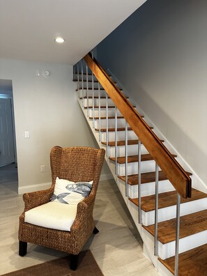 Staircase leads to a cozy seating area with a wicker armchair and cushion.