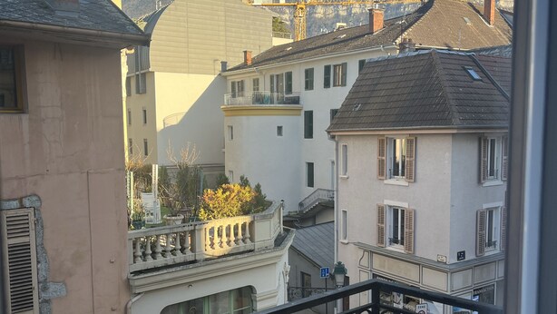 Un balcón con barandilla de hierro forjado que da a un barrio residencial con casas, una calle y una montaña al fondo.