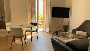 Una sala de estar moderna con comedor, un sofá de cuero negro, televisor y balcón con vistas.