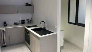Cocina compacta con lavavajillas, un lavabo y una encimera con hervidor y utensilios.