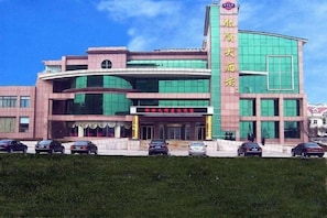A multi-story building with a prominent entrance, a vertical sign with text, and a parking lot with several cars. - Yintan Hotel (Rushan)