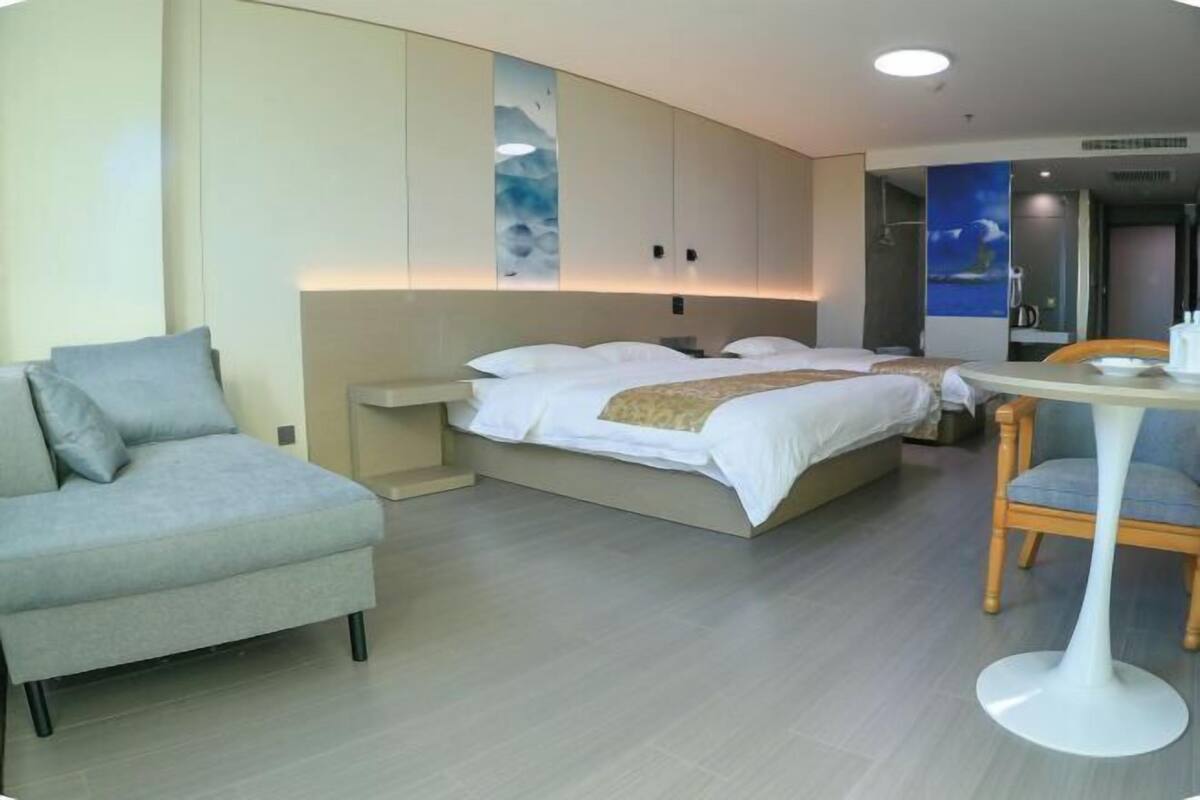 Una habitación de hotel moderna con una cama, un sofá gris, una mesita y una obra de arte colgada en la pared.