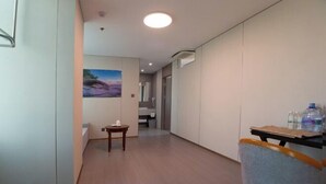 A hallway with a wooden floor, a chair, a small table with a cup, and a painting on the wall.