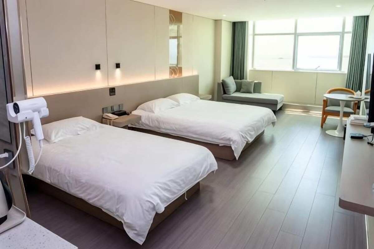 A hotel room with two beds, a desk, a chair, a small table, and a window.