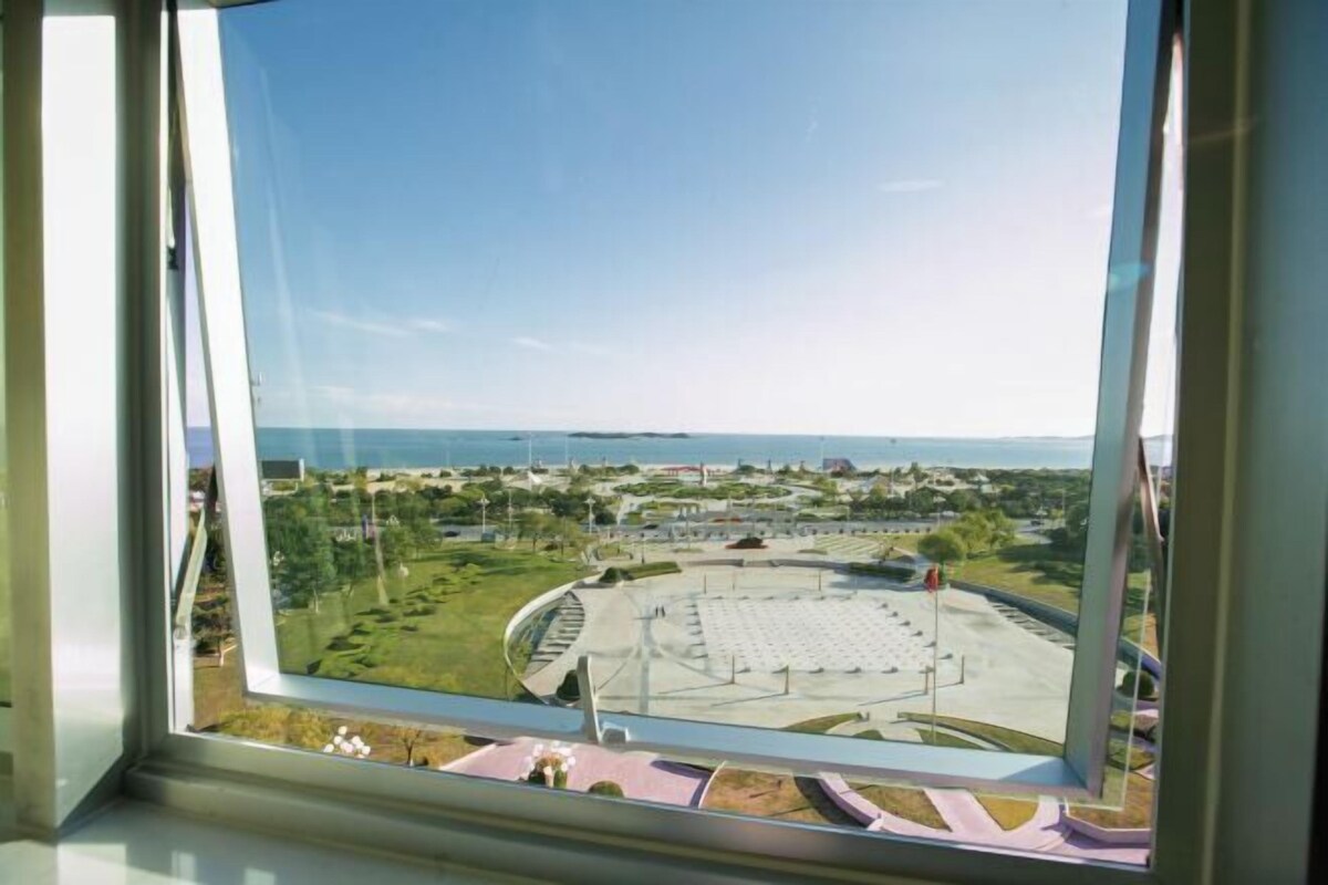 A view from a window of a circular building with a central open space, surrounded by greenery and a clear sky.