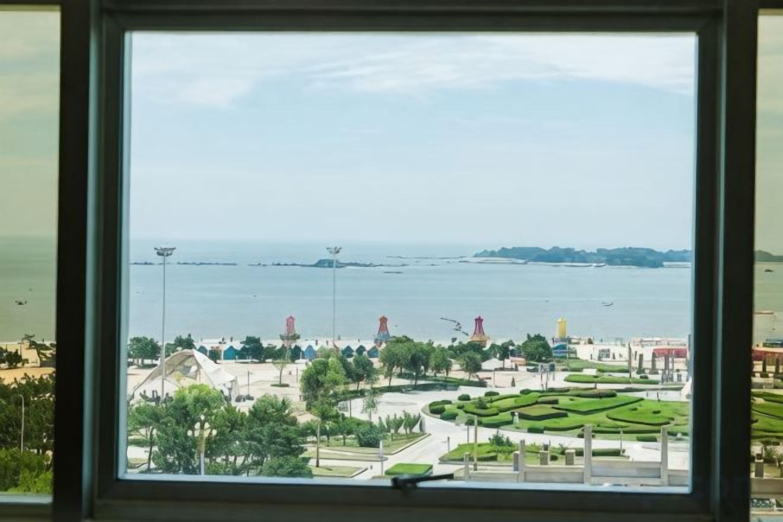 A view through a window of a landscaped area with pathways, trees, and a distant body of water.