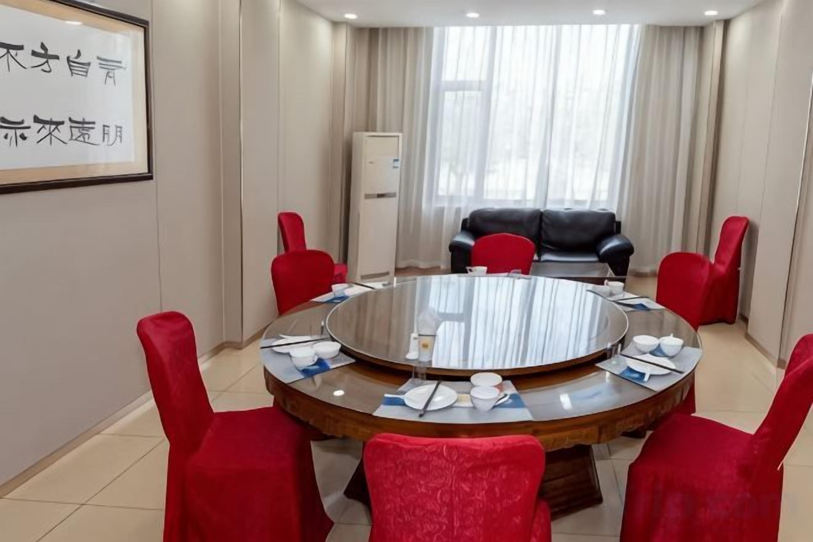 Uma sala de conferência com uma mesa redonda, cadeiras vermelhas e um sofá preto.
