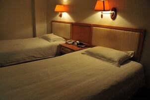 Habitación de hotel con dos camas individuales, cada una con cabecero de madera y mesita de noche con lámpara.