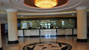 A hotel lobby with a reception desk, large columns, a chandelier, and a circular floor design.