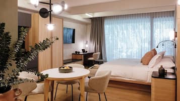 Una habitación de hotel moderna con cama, mesita de noche, lámpara y un área de comedor con sillas y mesa.