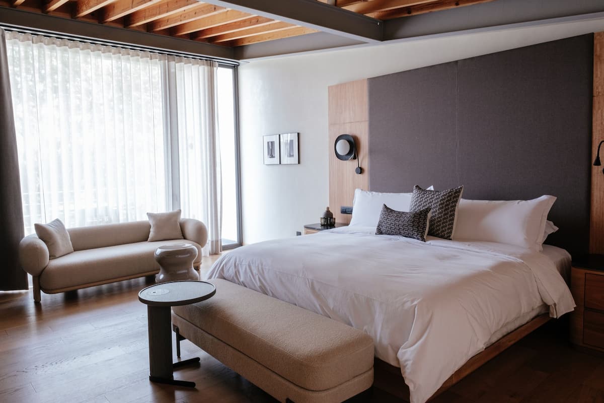 Un dormitorio moderno con una cama grande, un sofá, una mesita y una mesilla de noche.