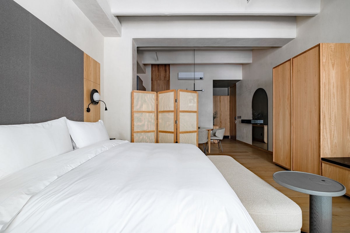 Una habitación de hotel moderna con una cama grande, una mesita redonda y un armario.