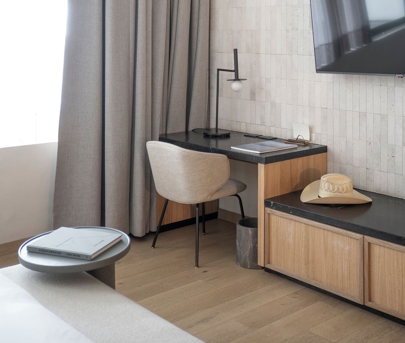A modern kitchen with a wooden cabinet, a black countertop, a chair, a small trash bin, and a flat-screen TV mounted on the wall.