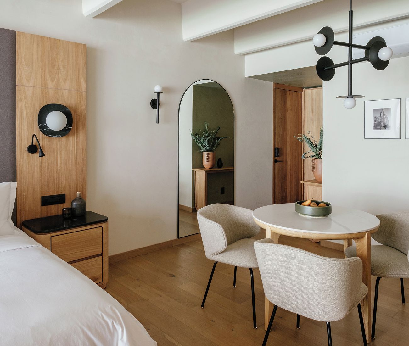 Une chambre d’hôtel moderne comprenant un lit, une table de chevet, une lampe, une table de salle à manger ronde avec des chaises et un miroir.
