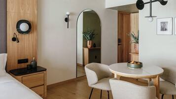 Une chambre d’hôtel moderne comprenant un lit, une table de chevet, une lampe, une table de salle à manger ronde avec des chaises et un miroir.