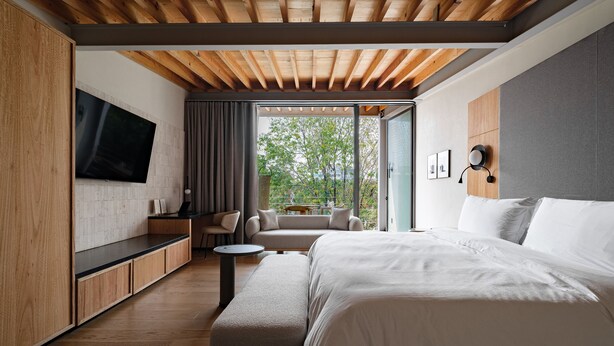 Ein modernes Schlafzimmer mit einem großen Bett, einem an der Wand montierten Fernseher, einer Couch und einem Esstisch.