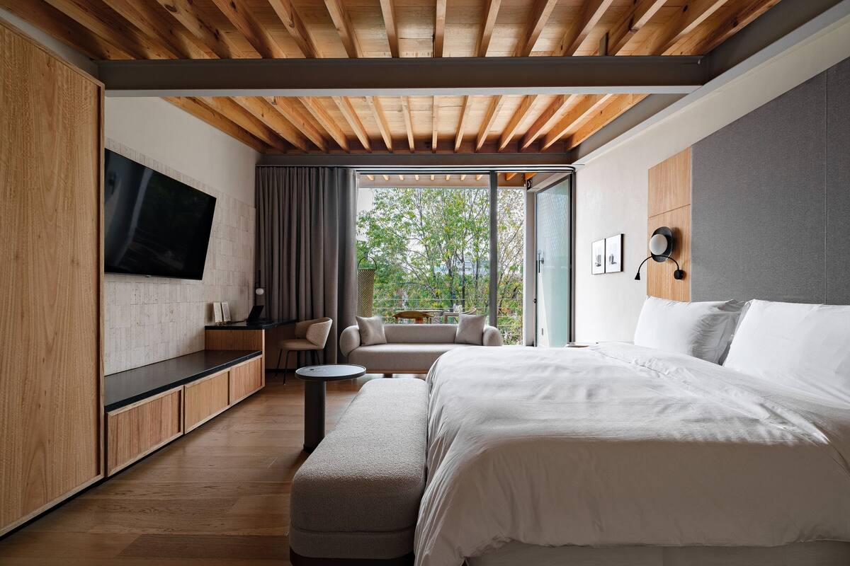 Un dormitorio moderno con una cama grande, un televisor montado en la pared, un sofá y una mesa de comedor.