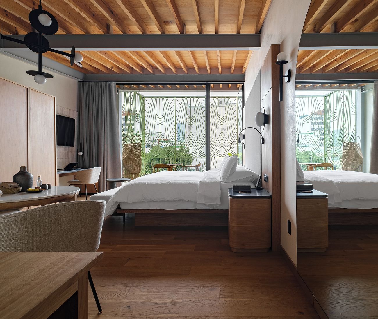 Habitació d'hotel moderna amb sostre de fusta, dos llits, un escriptori i vistes a vegetació a través de grans finestres.