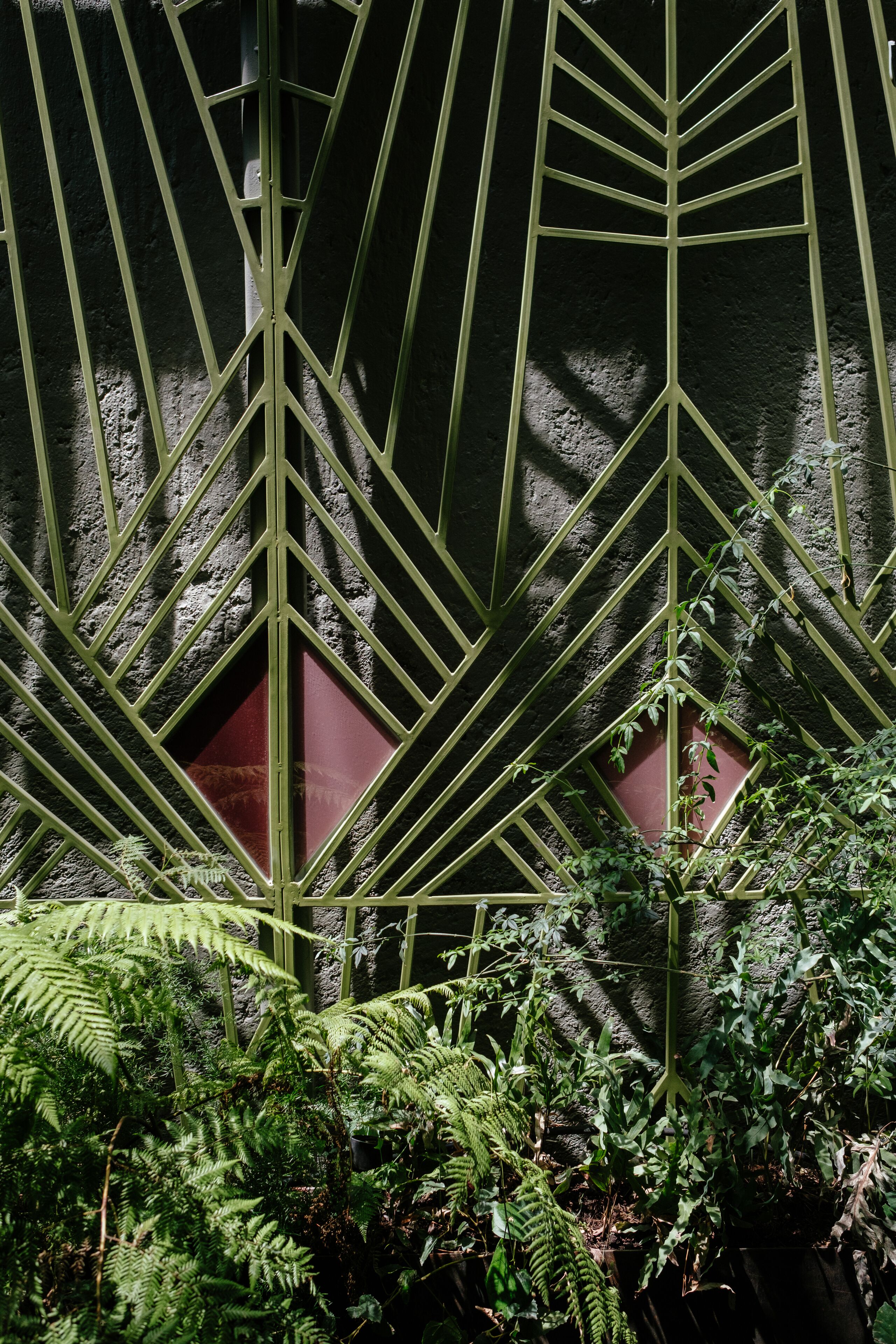 Une structure métallique aux formes géométriques, ornée d’un motif décoratif, et entourée d’un feuillage verdoyant et luxuriant.