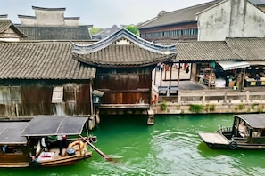 Un bâtiment traditionnel en bois, doté d’un toit en tuiles, bordé d’un canal, et devant lequel est amarré un petit bateau.