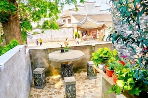Un patio con un edificio tradicional, una mesa de piedra y plantas en macetas.
