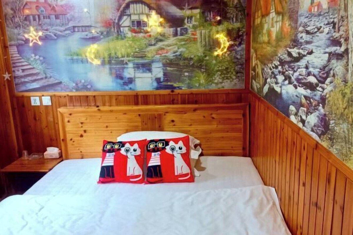 Une pièce aux murs lambrissés, avec un lit, deux oreillers ornés de personnages de dessins animés et une fresque représentant un paysage pittoresque.
