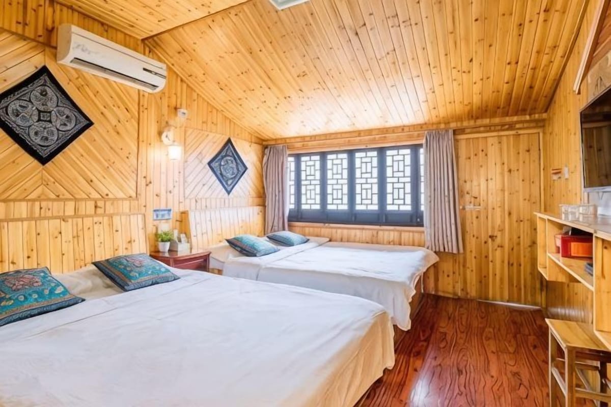 Une chambre dans un chalet en bois, avec deux lits, une fenêtre ornée d’un treillis décoratif et une étagère sur laquelle sont posés divers objets.