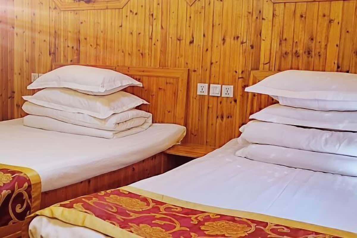 Una habitación con paredes revestidas de madera, dos camas con ropa blanca y una colcha roja y dorada en una de ellas.