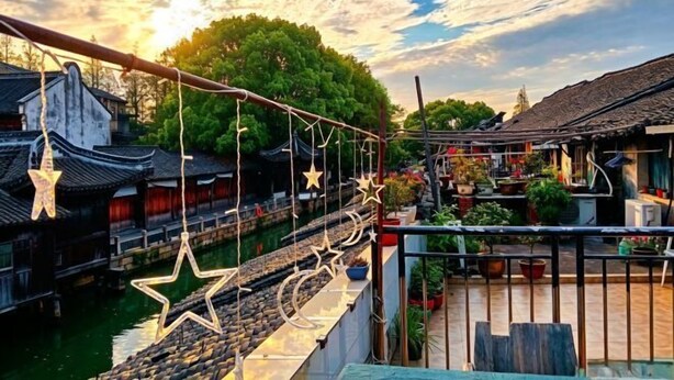 Une cour traditionnelle chinoise avec un pont en bois, des plantes en pot et une vue sur la rivière.