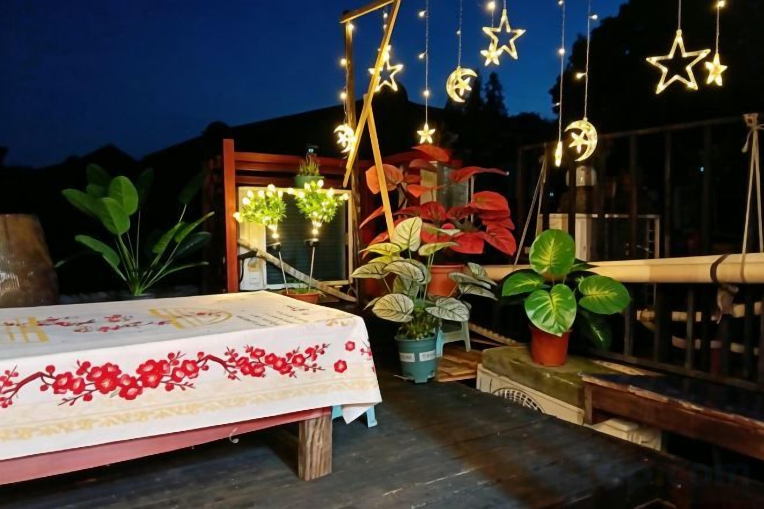 Un patio con una mesa lista para comer, plantas en macetas e iluminación colgante con forma de estrella.