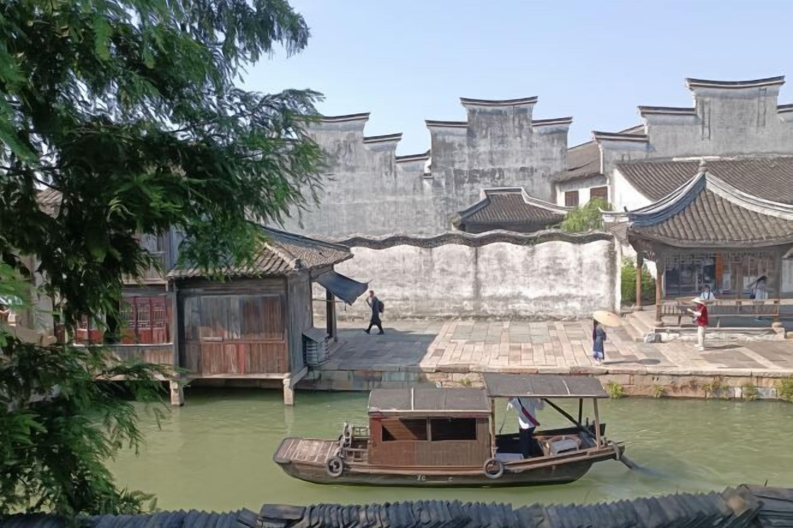 A traditional wooden boat on a river, surrounded by old-style buildings with tiled roofs.