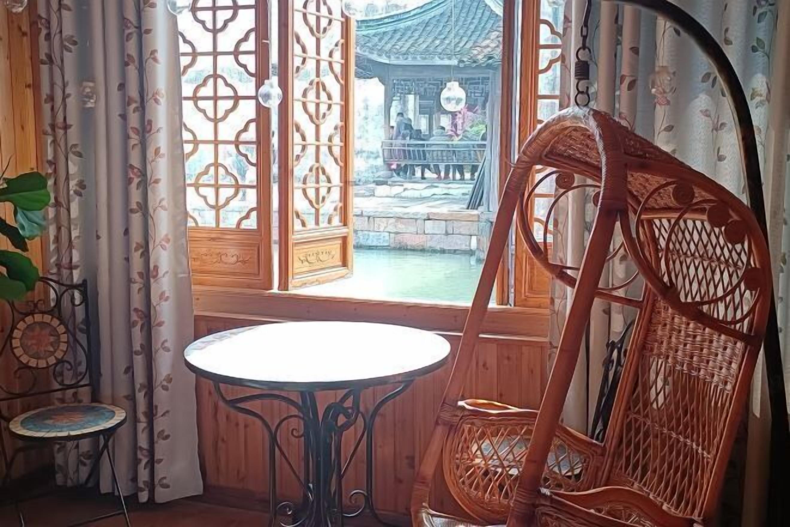 A wooden room with a traditional Chinese window, a round table, and a wicker chair.