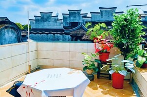 Una terraza en la azotea con una mesa, plantas en macetas y arquitectura china tradicional al fondo.
