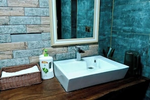 Un baño con lavamanos blanco, un espejo y una pared de piedra.
