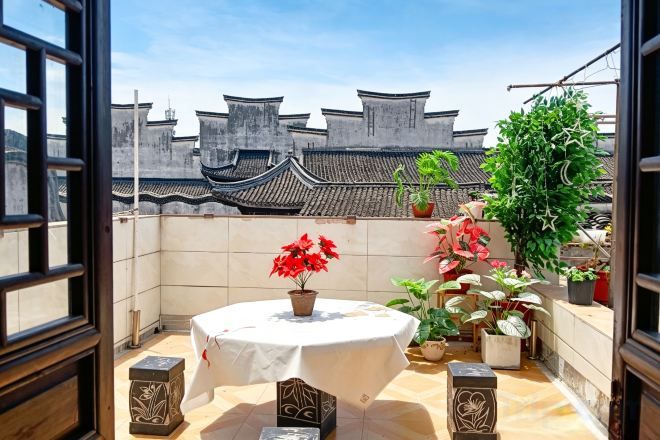 Un balcón con una mesa redonda, plantas en macetas y arquitectura tradicional china al fondo.