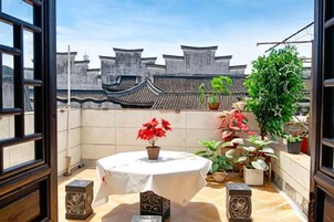 Un balcón con una mesa redonda, plantas en macetas y arquitectura tradicional china al fondo.
