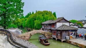 Un bateau en bois traditionnel sur une rivière, un pont de pierre et un bâtiment en bois avec un toit en tuiles.