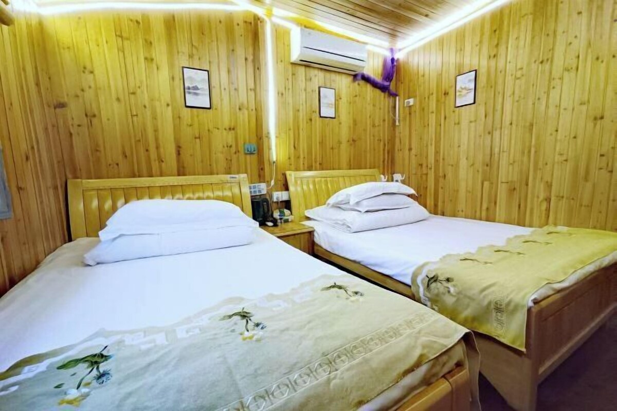 Une chambre avec deux lits en bois, chacun agrémenté de draps blancs et de motifs floraux. On y trouve des tables de chevet avec des lampes et un climatiseur fixé au mur.