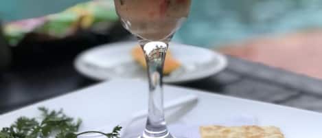 A seafood salad in a glass, garnished with lettuce, tomato, and a slice of orange, served with flatbread on a table by a pool.