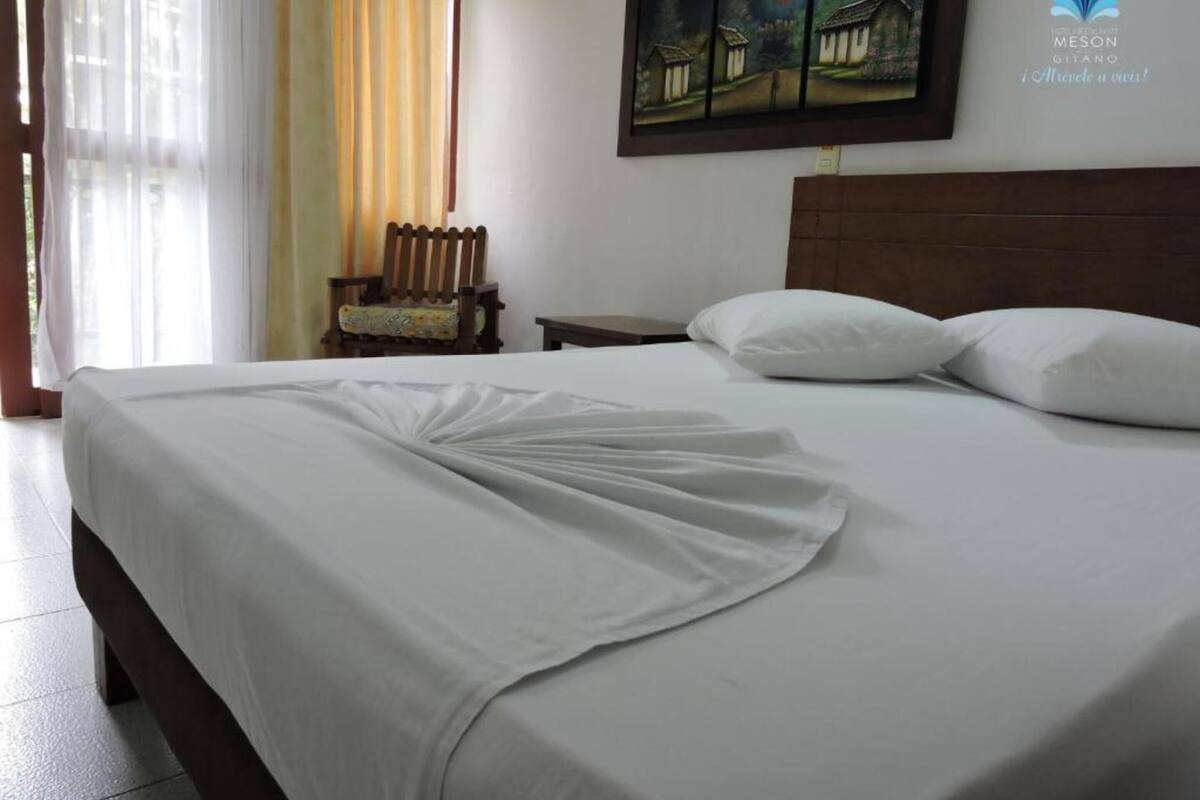 A neatly made bed with white linens, a wooden headboard, and a painting above it.