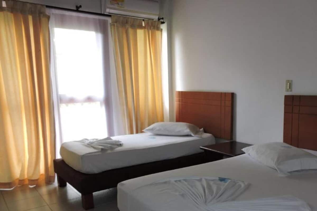 A hotel room with two beds, a wooden headboard, and a window with curtains.